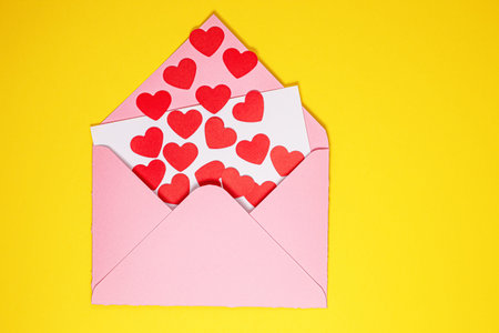 Valentines Day card. Paper red hearts fly out of pink paper envelope on yellow background . Paper...