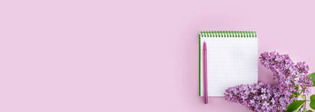 Lilac branch and Notepad on a pink background. notebook with bright lilac. Postcard for loved ones, relatives, friends and colleagues. Spring background. Long wide banner. Top view with copyspaceの写真素材
