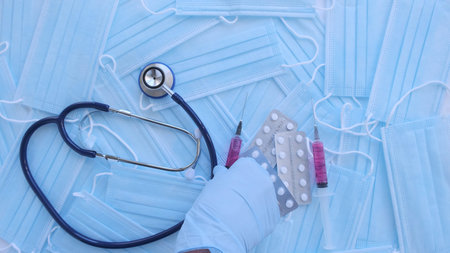 The doctors glove hand puts pills and syringes on table. Top view of face masks on surface. Medical supply mask to protect from infectious covid-19の写真素材