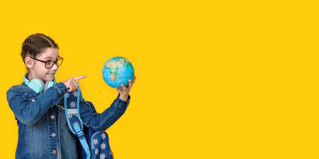 Young school teen kid girl 8-9 years old with backpack hold in hand globe world isolated on yellow background children studio portrait Education travel abroad lifestyle concept. Long wide bannerの写真素材