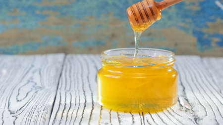 The glass jar with fresh honey on the rustic background. Flowers on the table. Honey dripping from honey dipper in glass jar. Healthy food concept, diet. Honey backgroundの写真素材