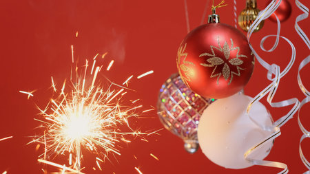 New Year multicolored balls and Sparkler Bright burning Christmas light on red background. Merry...