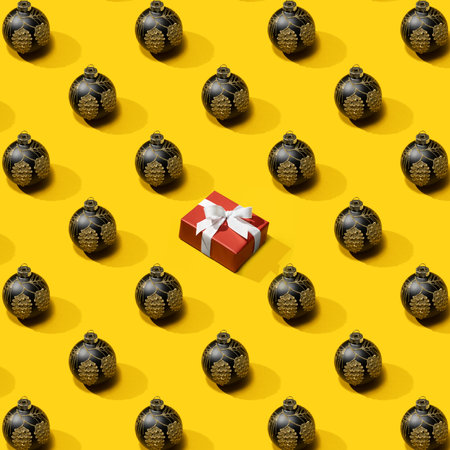 New Years pattern from black christmas ball decoration with Gift box on yellow background. Christmas pattern made of New Year ball. Minimal Christmas or New Year concept.の写真素材