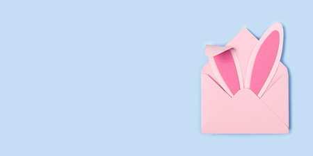 Happy Easter. Bunny rabbit ears made of pink paper in pink envelope on blue background. Easter greeting card with envelope. Happy Easter minimal concept with copy space for text. Banner. Flat layの写真素材
