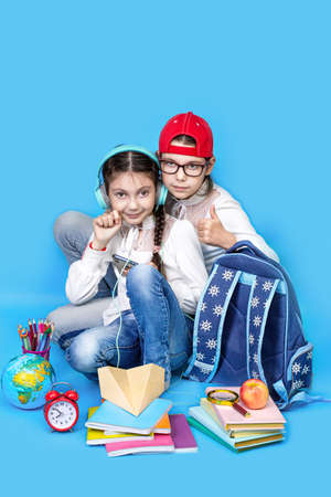 Back to school. Portrait of school girl, Girls sisters in glasses sit floor on blue background. smiling school girl sitting near globe backpack school books. Schoolchild in class. education conceptの写真素材