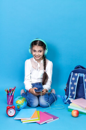Back to school. Portrait of school girl in glasses sit floor on blue background. smiling school girl sitting near globe backpack school books. Schoolchild in class. Child education conceptの写真素材
