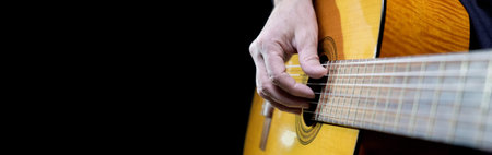 Guitarist playing acoustic guitar on black background, selective focus. A male musician plays the...