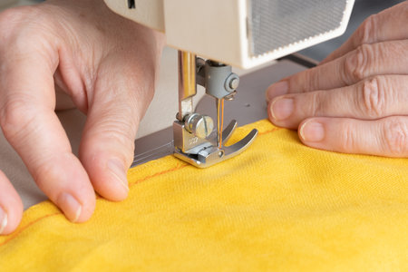 Hands of seamstress sewing with a professional machine, embroiders sews on grey fabric. man seamstress sitting and sews on sewing machine in studio. Sewing workshop. Concept of Factory, Homeの写真素材