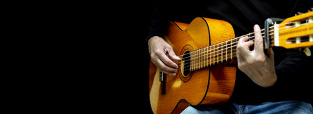 Guitarist playing acoustic guitar on black background, selective focus. A male musician plays the guitar. cover for online courses learning at home. A man playing guitar. Long wide banner, copy spaceの写真素材