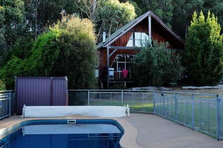 An outdoor pool in front of a wooden country cottage surrounded by trees and bushesの写真素材