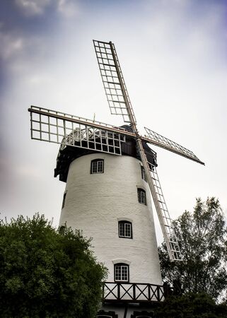 Old white windmill tower on a cloudy day between two treesの写真素材