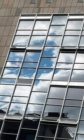 Facade view of glass building where the sky and clouds are reflected. Modern office building made of...