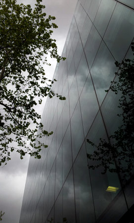 Bottom view of glass building where the sky is reflected. Cloudy day. Modern office building.