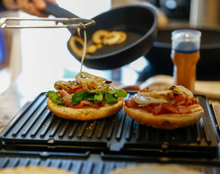 Unfocused woman cooking burgers at home. Meat burgers with bacon, cheese, onion and bread.の写真素材