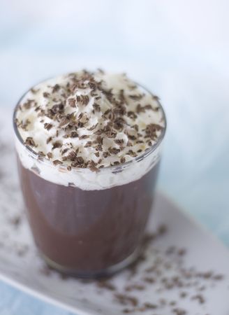 Cup of chocolate pudding with whip cream topping and chocolate shavings on long dessert plate and light blue background.の写真素材
