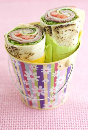 Wrap sandwiches with salami, red peppers, lettuce& cheese in a colorful pail on pink background.の写真素材