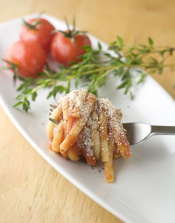 Linguine in tomato sauce and parmesan, coiled around fork on tasting plate with fresh herbs and cherry tomatos in background.の写真素材