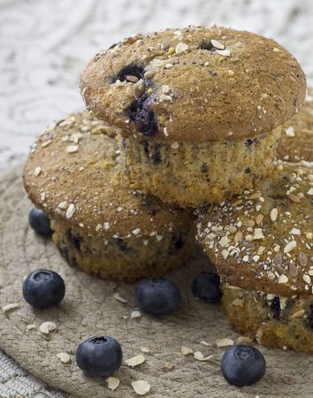 Three blueberry muffins on beige mat with oatmeal flakes and fresh blueberries on lace tablecloth.の写真素材