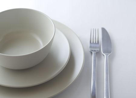 Table place setting with bowl, two plates, fork and knife on white background.の写真素材