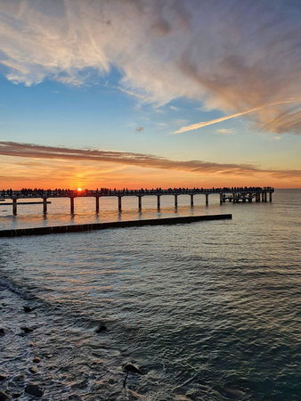 Beautiful sunset sky over calm Baltic Sea with silhouettes of pier and wooden breakwaters on a...