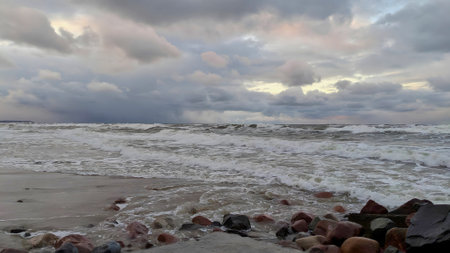 Scenic seaside landscape on severe Baltic sea shore with stormy waves rolling on empty beach under dramatic sky with storm clouds at winter dusk. With no people desolate seascape.の写真素材
