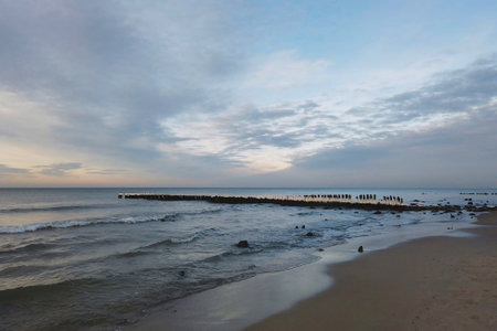 Scenic seaside landscape on empty sandy shore of severe Baltic sea with calm waves rolling on old wooden breakwater under cloudy sky at winter morning. No people tranquil seascape.の写真素材