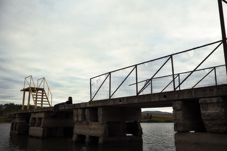 a young lonely teenage girl lies from afar looks at a gloomy photo into the distance and is renounced alone with herself thinks and is bored frustrated on a pier by the water sits on a pier in the evening. High quality photoの写真素材