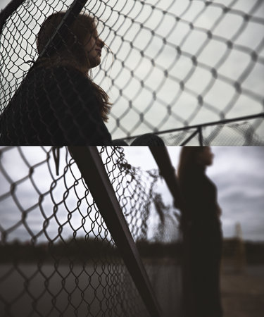 teenage girl young lonelynear the iron fence bulling looks at a gloomy photo into the distance and the renunciate thinks alone with herself and is bored upset on the pier by the water sits on the pier in the evening. High quality photoの写真素材