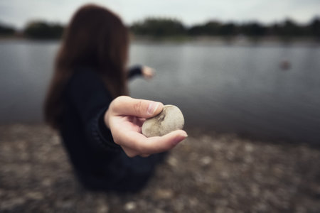a teenage girl stands alone in nature trying to cope with anger and find strength in the evening under the wind throws a stone into the water looks thinking about fate is not easy and hard. High quality photoの写真素材