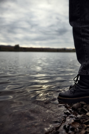 an abandoned teenager a man stands by the water, looks and reflects on the hard life of shoes in the...
