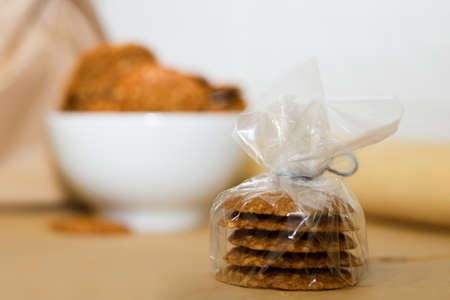In the foreground are five sesame cookies wrapped in cellophane. In the background there is a white plate and a brown paper bag out of focus. Homemade baking.の写真素材