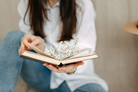 A close-up photo of an open book on the sheets of which white small flowers lie, and the girl's fingers turn over the book. No face, only part of the figure. Literature. Mood.の写真素材