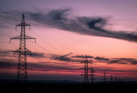 High voltage poles stand against the sunsetの写真素材