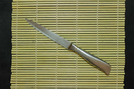 The metal knife lies on the sushi mat. Metal colored knife.の写真素材