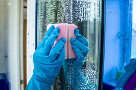 The girl cleans the mirror with a special liquid and sponge. Cleaning the bathroom with cleaning products. Cleaningの写真素材