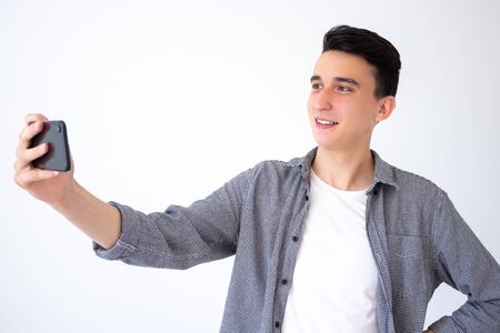 A positive, happy guy takes a photo on his phone or communicates via video link. Guy on a gray...
