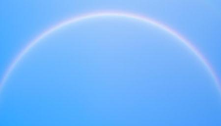 A bright rainbow arc stretches across a clear blue sky, showcasing the beauty of atmospheric optics and natural phenomenaの素材
