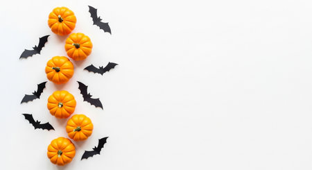 Top view of small orange pumpkins and black paper bats arranged vertically on white background for halloweenの素材