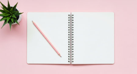 Top view of an open blank spiral notebook with a pink pencil and small potted succulent plant on pink backgroundの素材