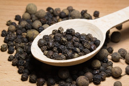 Grains of black pepper in a spoon on a wooden background