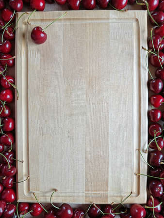 wooden rectangular background around which lies ripe cherriesの写真素材