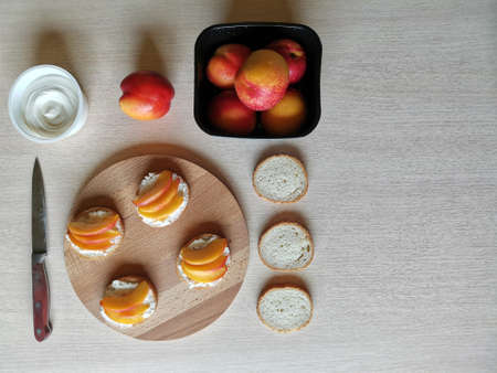 sandwiches with cream cheese, fresh nectarines slices on a serving wooden plank and ingredients.
