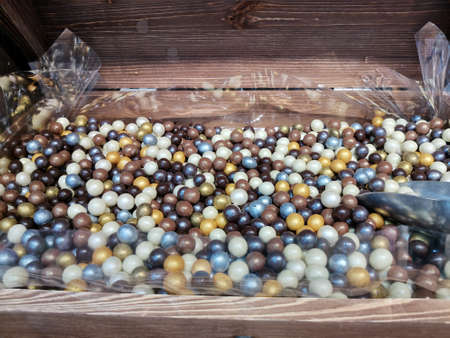 Multicolored candy nuts in chocolate glaze lie in a wooden chest