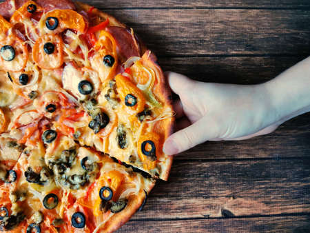 Womans hand takes a slice of pizza dark brown backgroundの写真素材