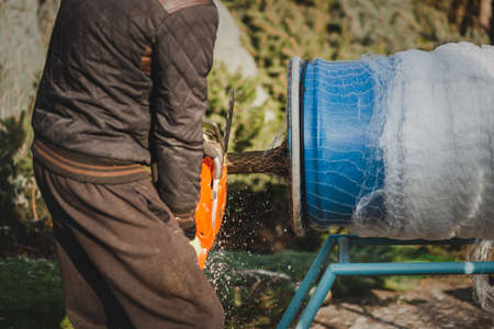 A man with a chainsaw in his hands pours water from a bucket into a bucket.の写真素材