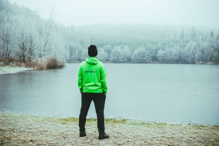 A man in a green jacket stands on the shore of a lake.の写真素材