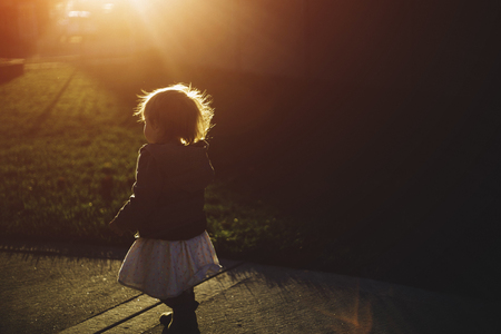 Little girl walks in the yard to the background lighting of the sun.の写真素材