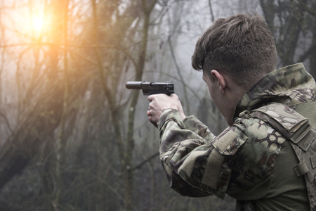 A guy with a gun takes aim in the woods