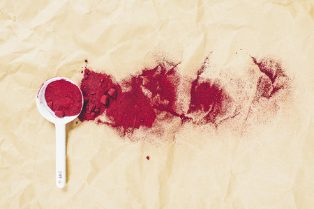 Red spice on white spoon scattered on the paper backgroundの写真素材