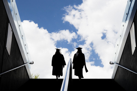 Silhouette of two students in a robe climb up the stairsの写真素材